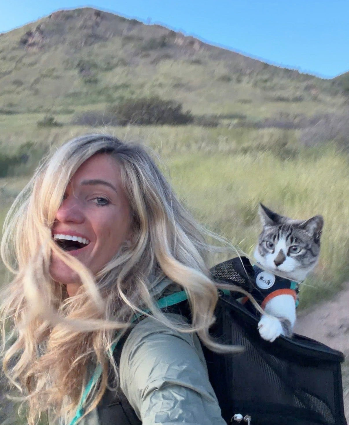 Woman hiking with a cat in a backpack against a mountainous background