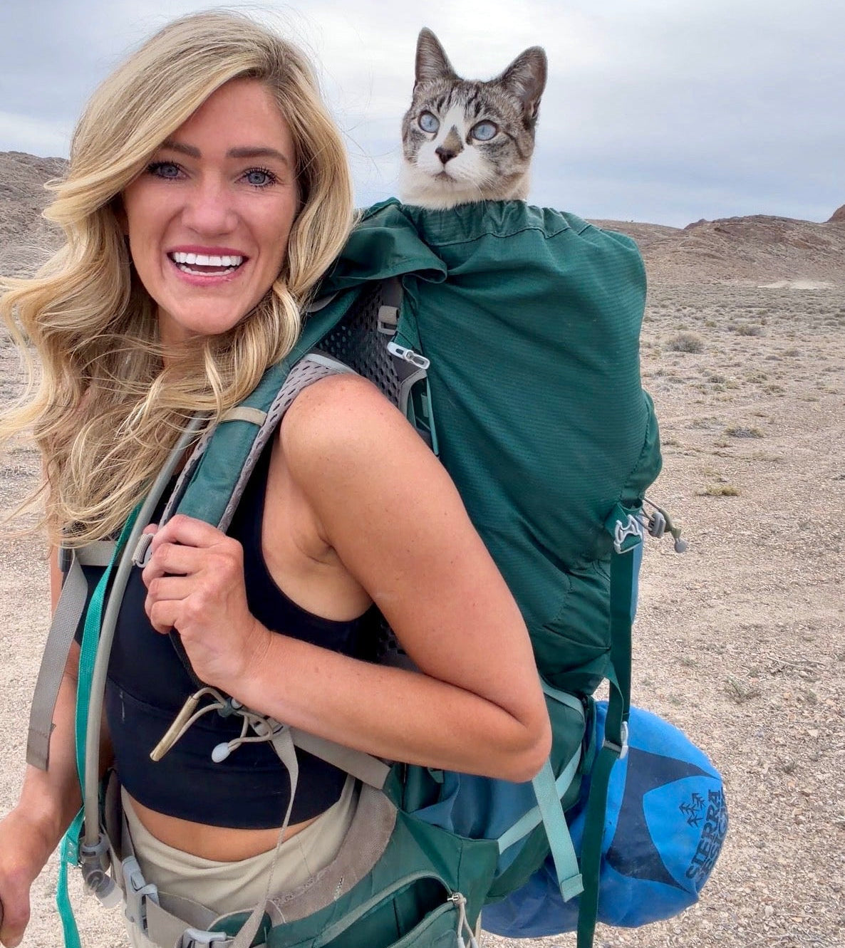 Woman hiking with a cat on her backpack in a desert landscape